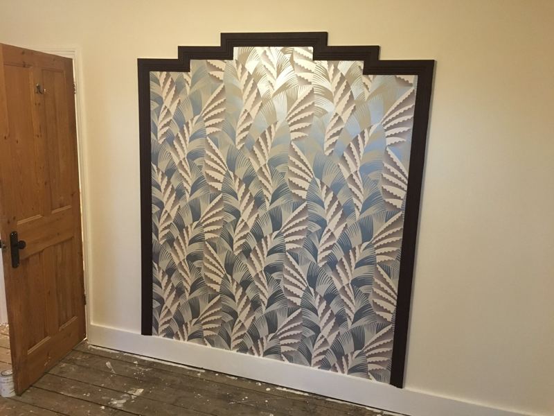 Patterned wallpaper panel with a dark stepped timber frame in a bedroom