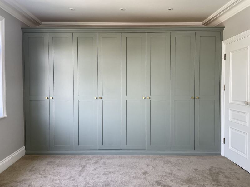 Full wall of fitted shaker wardrobes painted in Farrow and Ball Pigeon with brass knobs