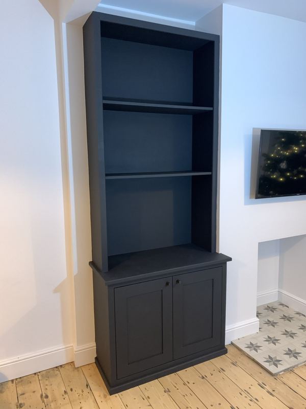 Fitted alcove unit with shaker-style cupboard doors and open shelves above, painted matt black