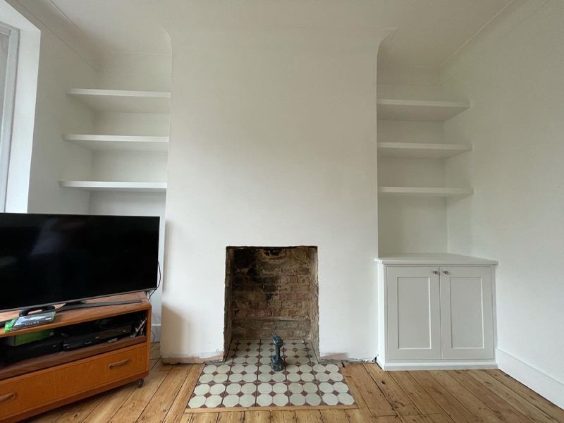 White floating shelves in both alcoves either side of a fireplace, with a fitted cupboard under one side